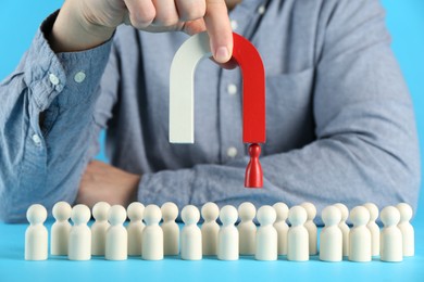 Photo of Man with magnet attracting red piece among wooden ones on light blue background, closeup