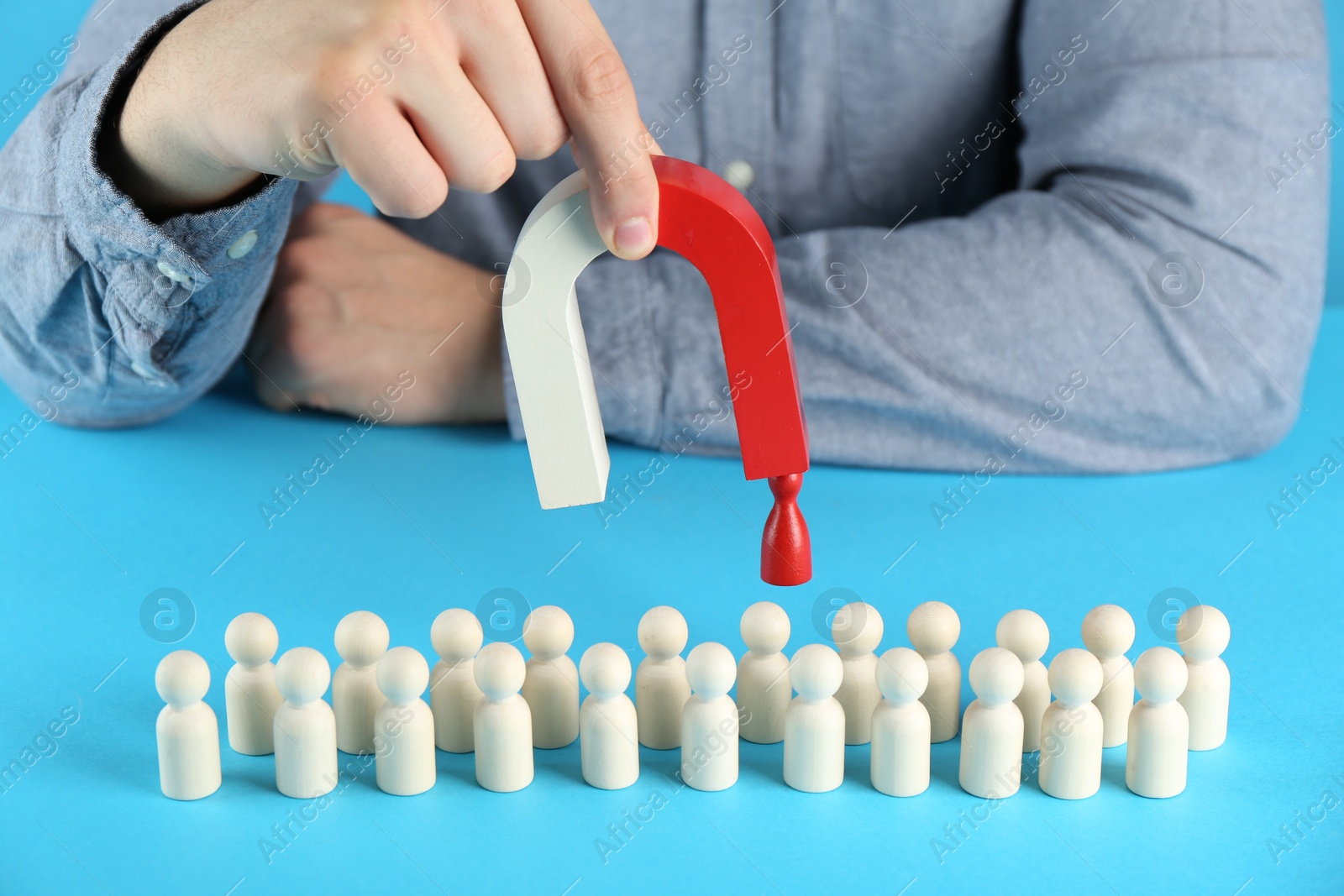 Photo of Man with magnet attracting red piece among wooden ones on light blue background, closeup