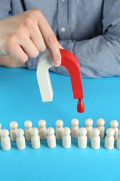 Photo of Man with magnet attracting red piece among wooden ones on light blue background, closeup