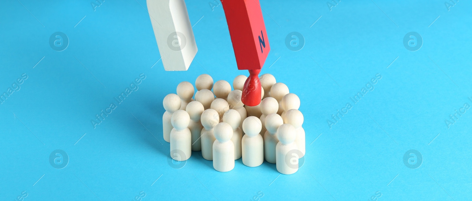 Photo of Attracting red piece among wooden ones with magnet on light blue background, closeup