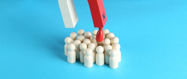 Photo of Attracting red piece among wooden ones with magnet on light blue background, closeup