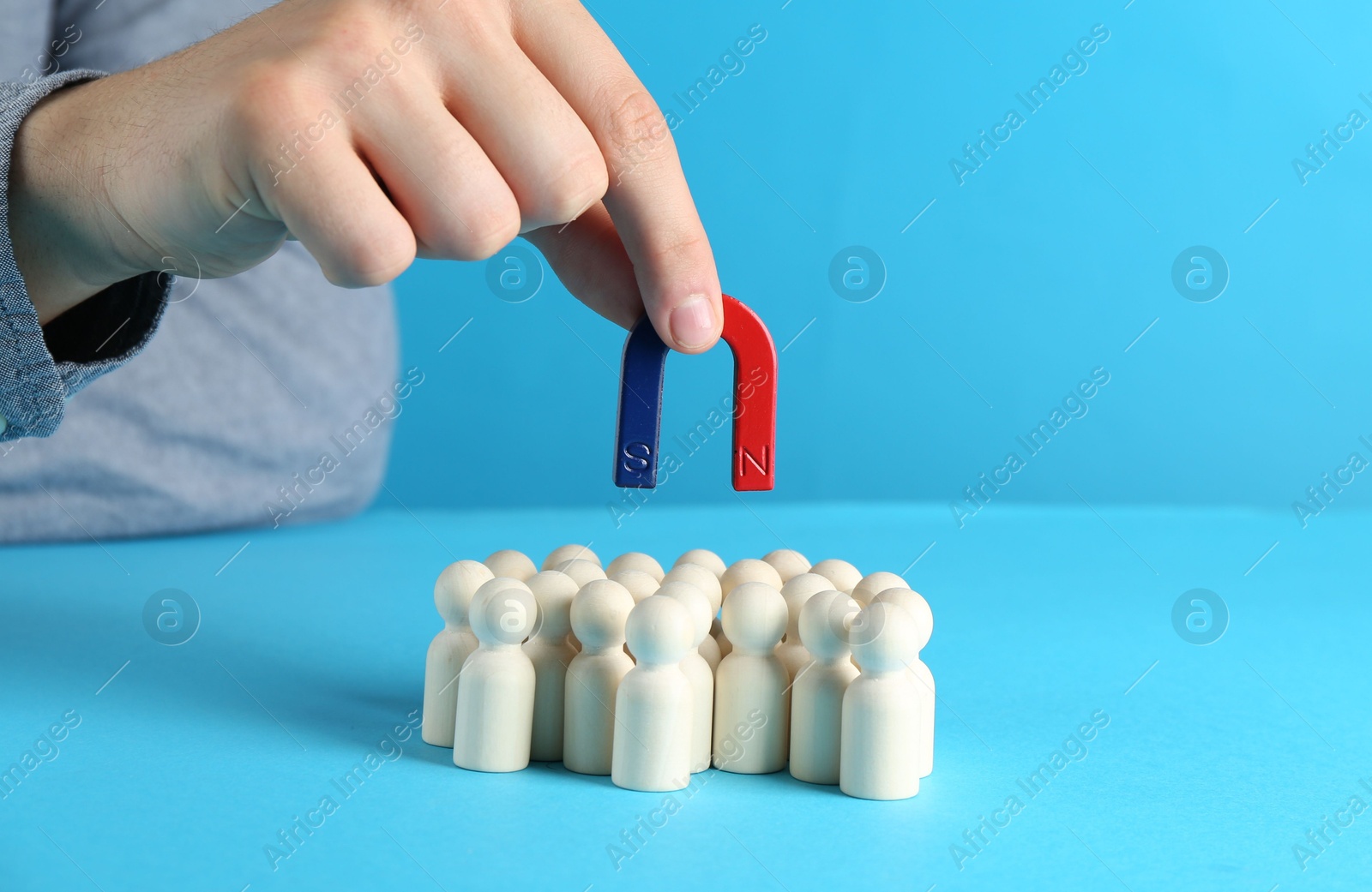 Photo of Man with magnet attracting wooden human figures on light blue background, closeup