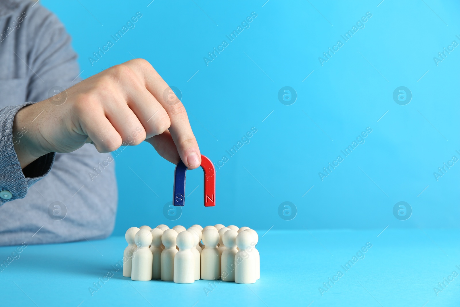 Photo of Man with magnet attracting wooden human figures on light blue background, closeup. Space for text