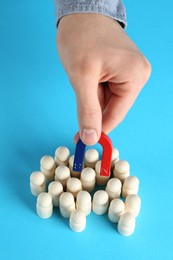 Photo of Man with magnet attracting wooden human figures on light blue background, closeup