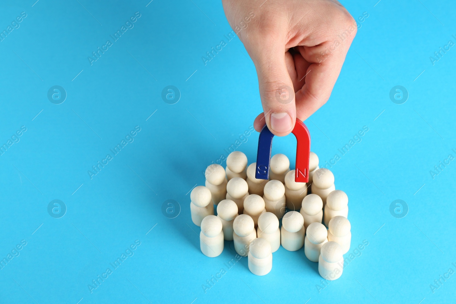 Photo of Man with magnet attracting wooden human figures on light blue background, closeup. Space for text