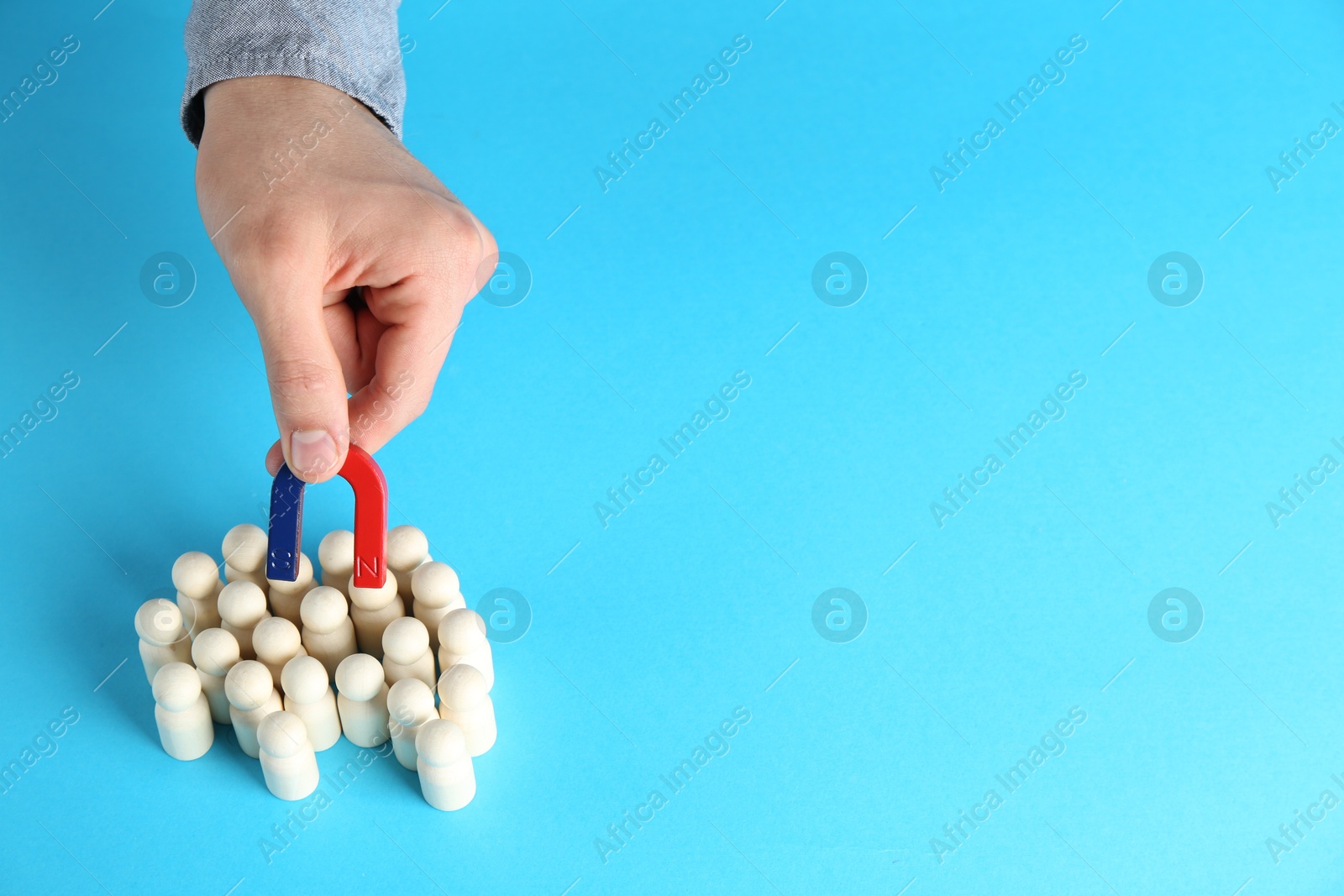 Photo of Man with magnet attracting wooden human figures on light blue background, closeup. Space for text