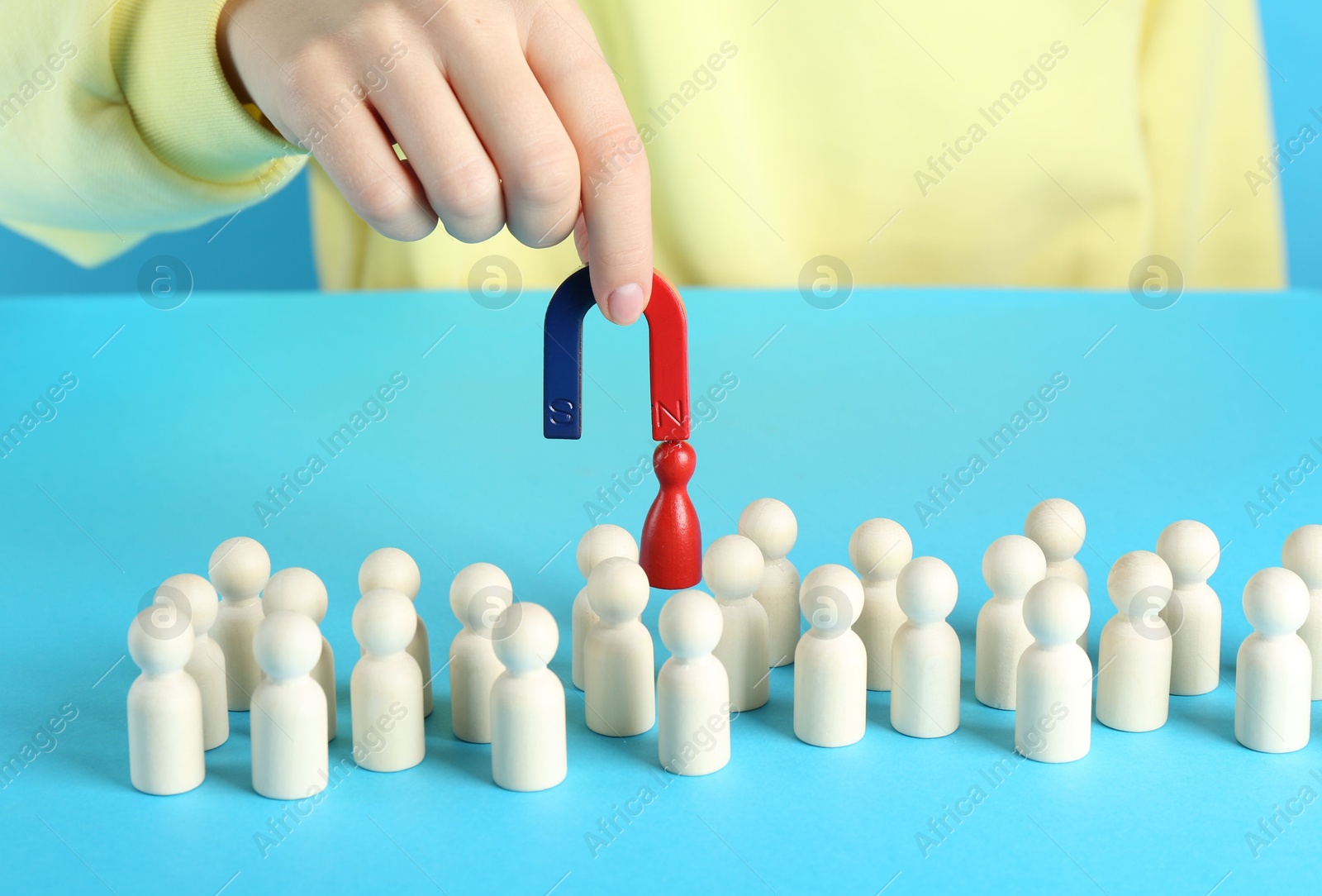 Photo of Woman with magnet attracting red piece among wooden ones on light blue background, closeup