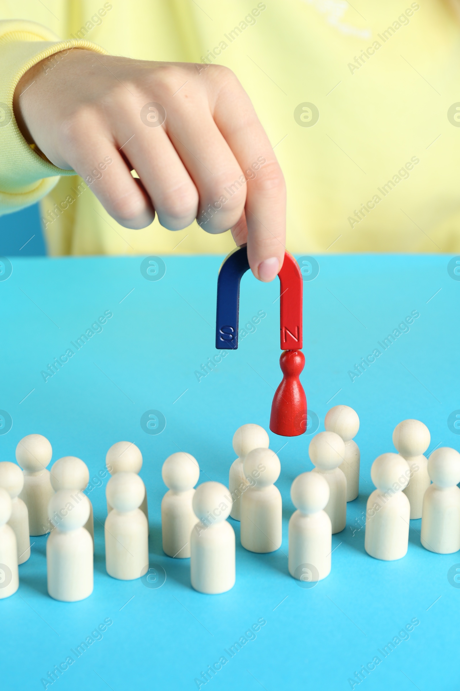 Photo of Woman with magnet attracting red piece among wooden ones on light blue background, closeup