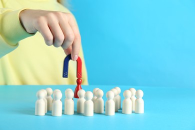 Photo of Woman with magnet attracting red piece among wooden ones on light blue background, closeup