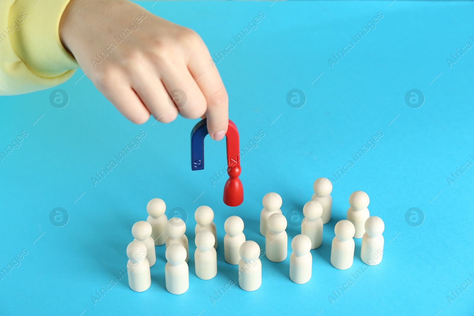 Photo of Woman with magnet attracting red piece among wooden ones on light blue background, closeup