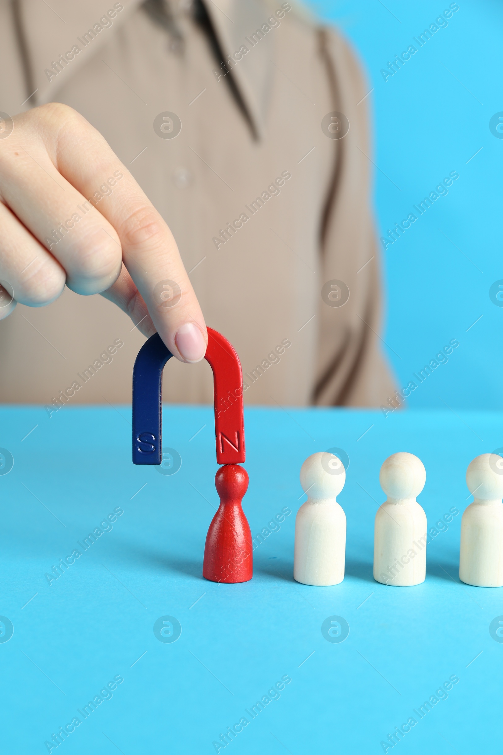 Photo of Woman with magnet attracting red piece among wooden ones on light blue background, closeup