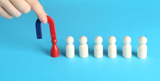 Photo of Woman with magnet attracting red piece among wooden ones on light blue background, closeup