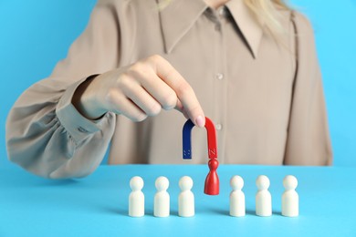 Photo of Woman with magnet attracting red piece among wooden ones on light blue background, closeup