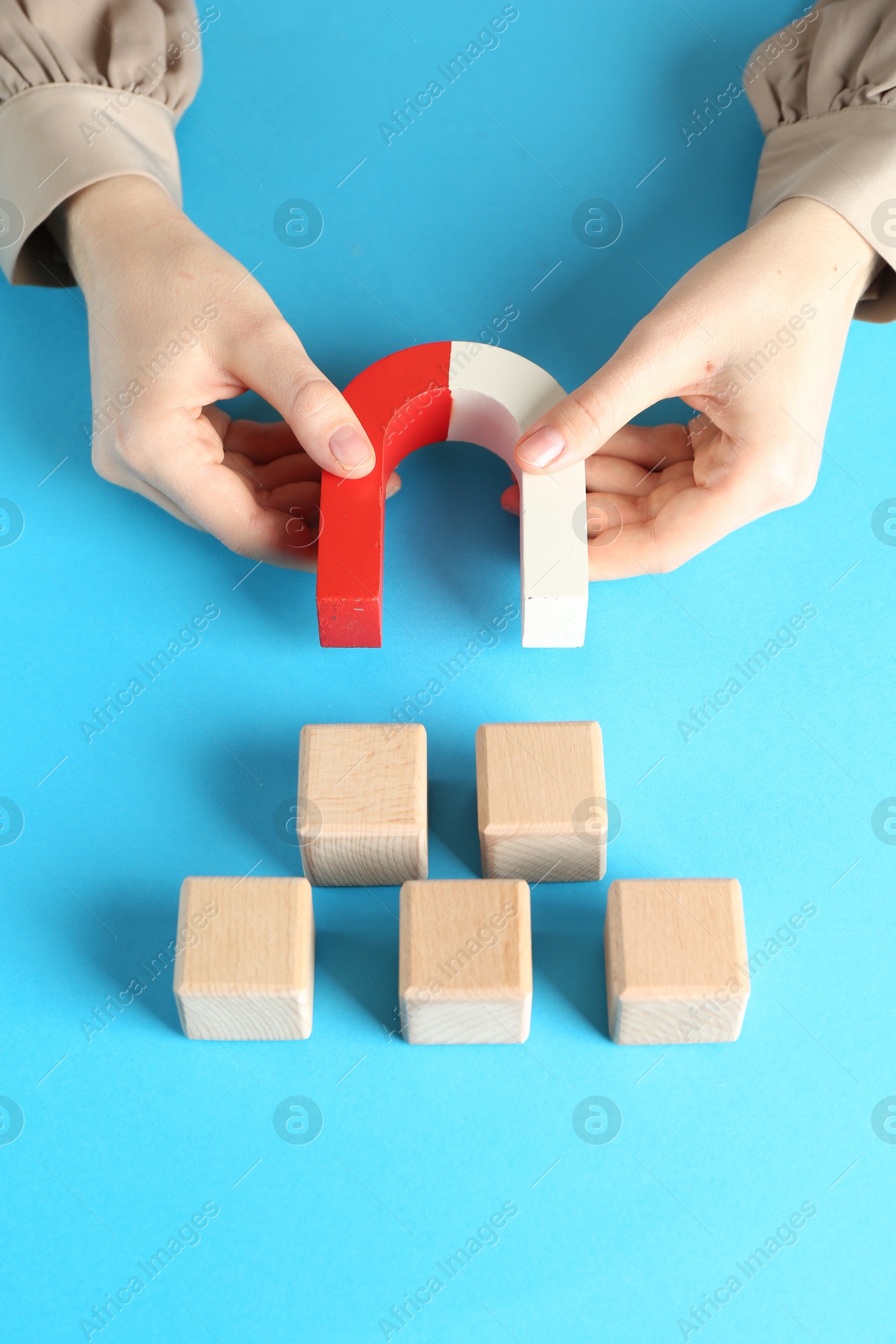 Photo of Woman with magnet attracting wooden cubes on light blue background, closeup