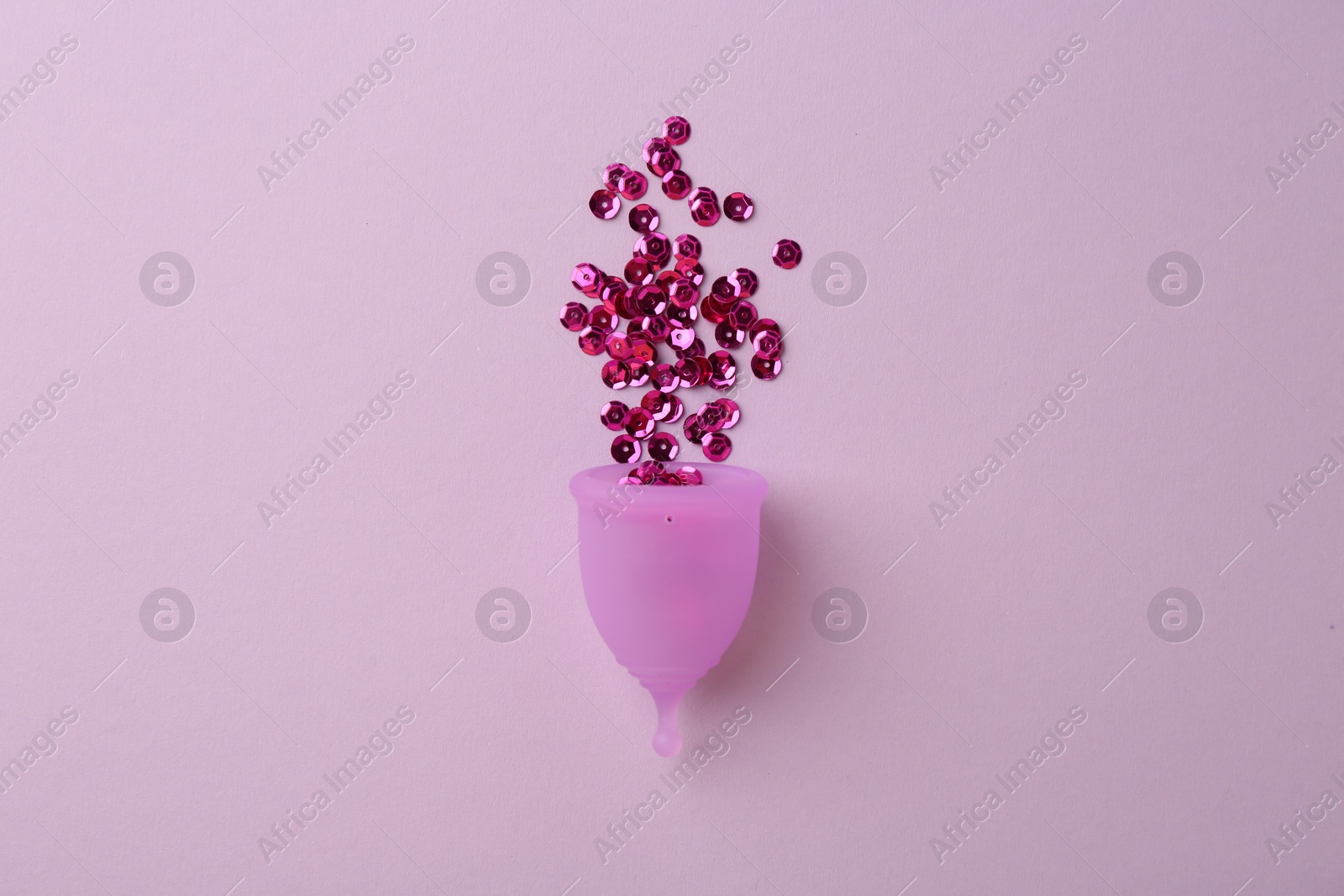 Photo of Menstrual cup with sequins on lilac background, top view