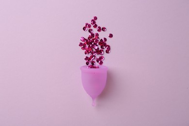 Menstrual cup with sequins on lilac background, top view