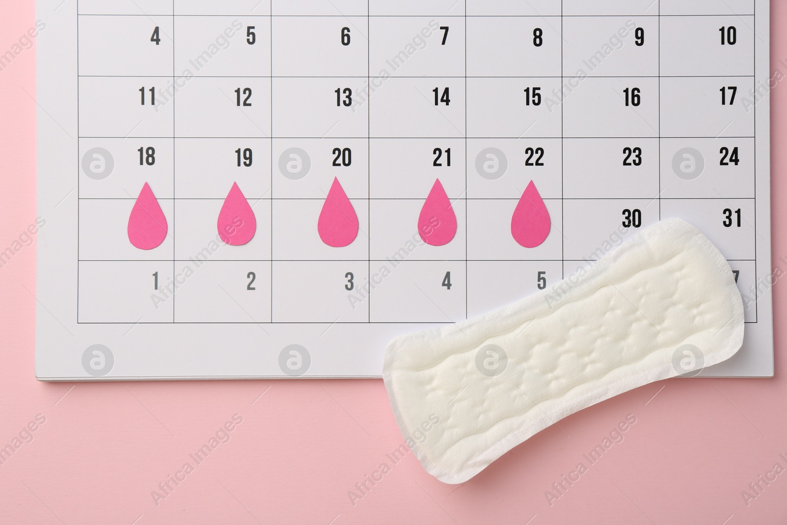 Photo of Calendar with marked dates and menstrual pad on light pink background, top view