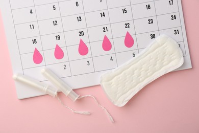 Photo of Calendar with marked dates, menstrual pad and tampons on light pink background, top view