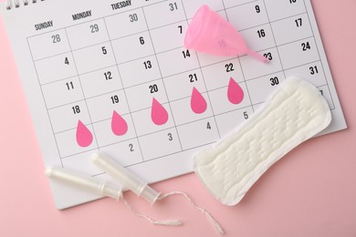 Calendar with marked dates, menstrual pad, cup and tampons on light pink background, top view