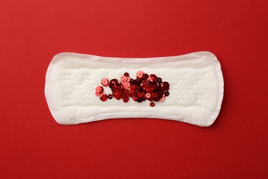 Photo of Menstrual pad with sequins on red background, top view