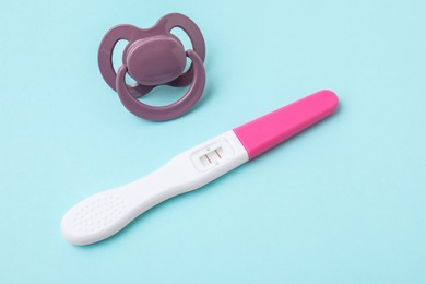 Photo of Pregnancy test and pacifier on light blue background, closeup