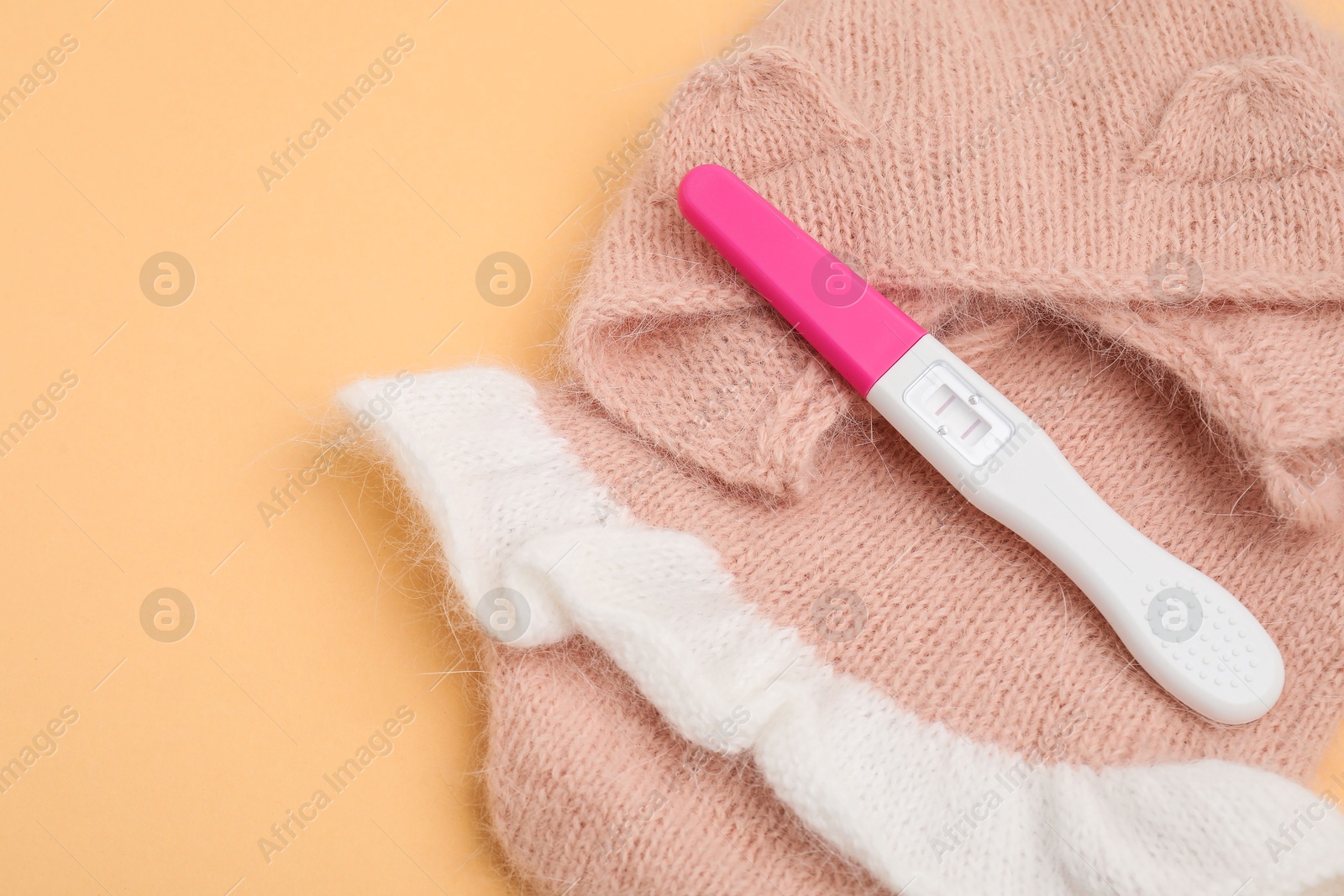 Photo of Pregnancy test and baby clothes on pale orange background, closeup