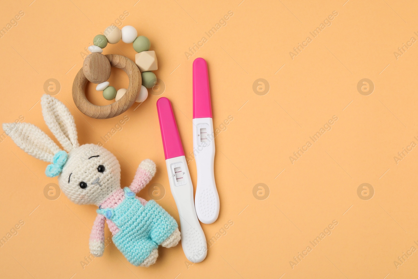 Photo of Pregnancy tests, baby rattle and toy bunny on pale orange background, top view. Space for text