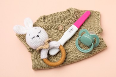 Photo of Pregnancy test, rattle, baby clothes and pacifier on beige background, top view