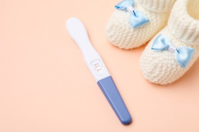 Photo of Pregnancy test and baby booties on beige background, closeup