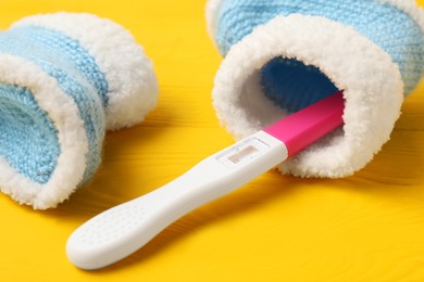 Photo of Pregnancy test and baby shoes on yellow wooden table, closeup