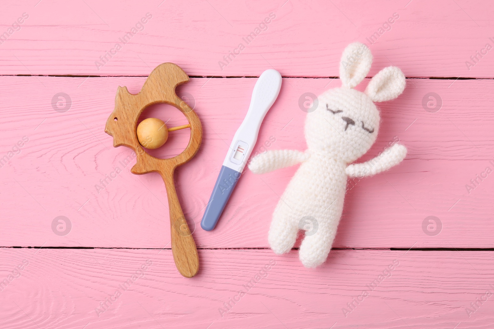 Photo of Pregnancy test and baby toys on pink wooden table, flat lay