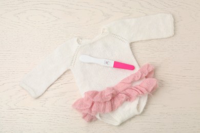 Photo of Pregnancy test and baby onesie on white wooden table, top view