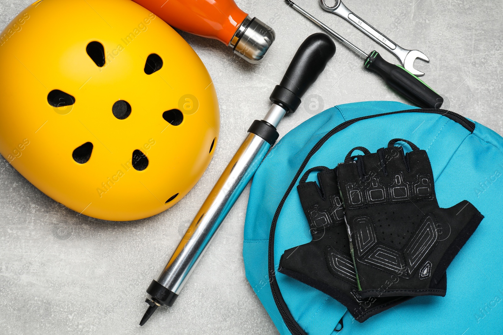 Photo of Bicycle helmet, backpack, gloves and other tools on light grey table, flat lay