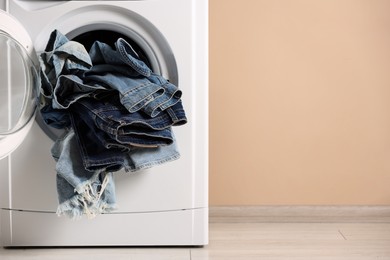 Photo of Washing machine with dirty jeans and other denim clothes indoors, space for text