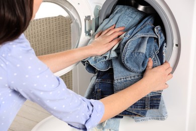 Woman putting dirty jeans and other denim clothes into washing machine, closeup