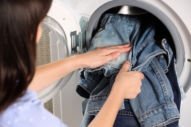 Photo of Woman putting dirty jeans and other denim clothes into washing machine, closeup