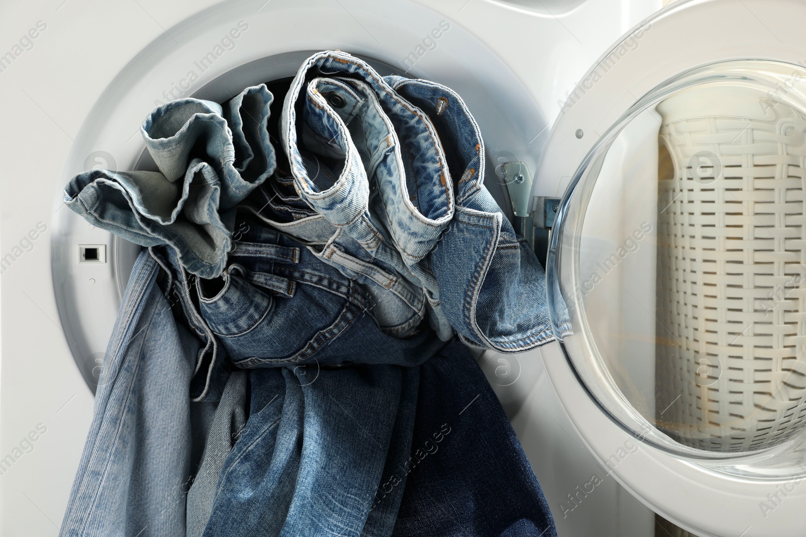 Photo of Washing machine with dirty jeans and other denim clothes indoors, closeup