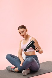 Young woman with percussive massager on mat against pink background