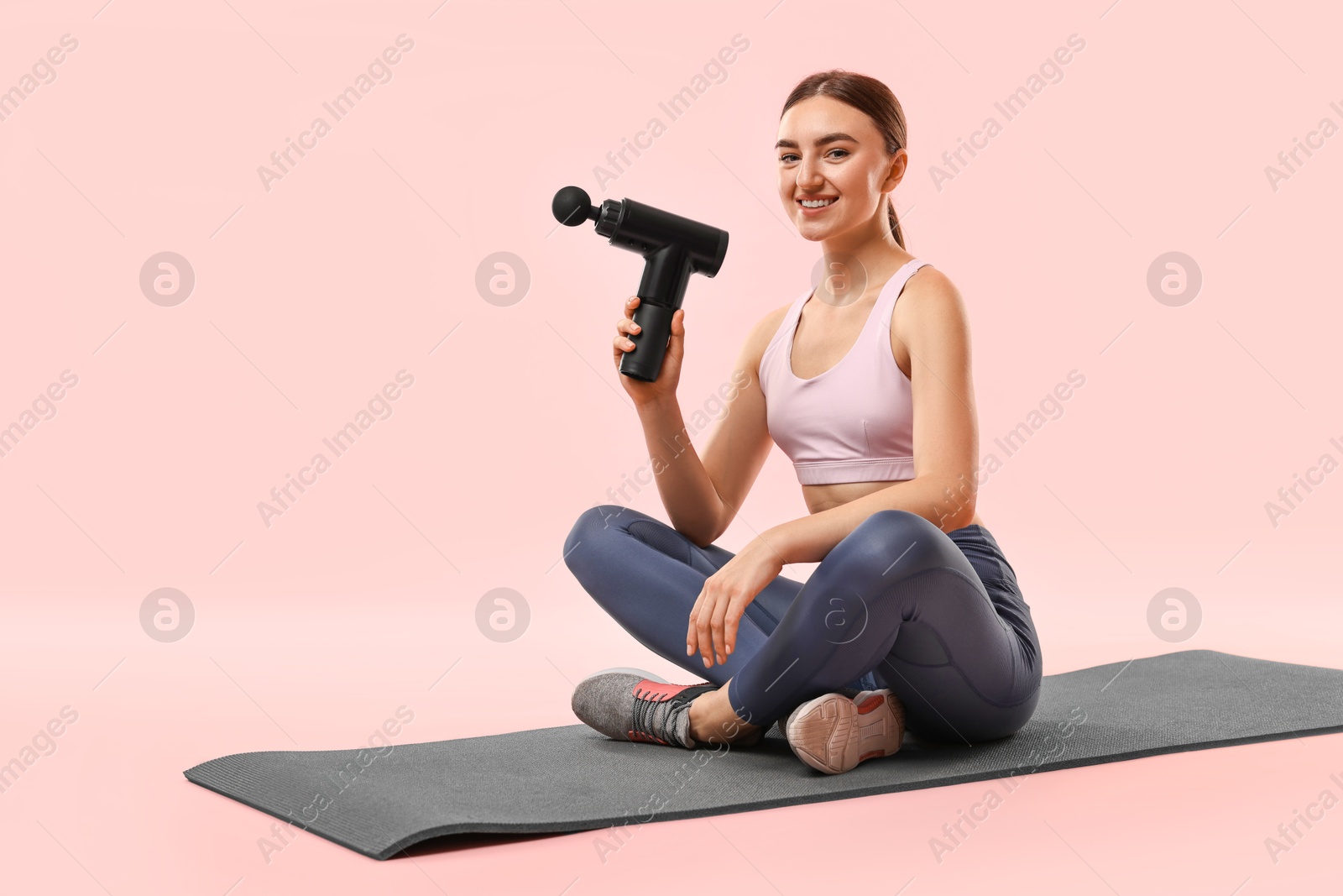 Photo of Young woman with percussive massager on mat against pink background