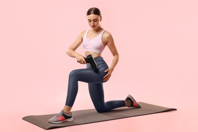 Photo of Woman using percussive massager to relax hip muscles on mat against pink background