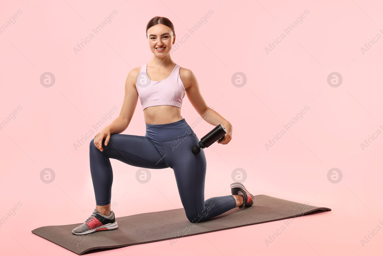 Photo of Woman using percussive massager to relax hip muscles on mat against pink background