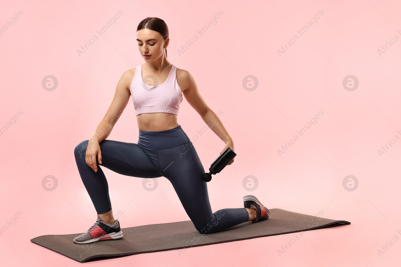 Photo of Woman using percussive massager to relax hip muscles on mat against pink background. Space for text