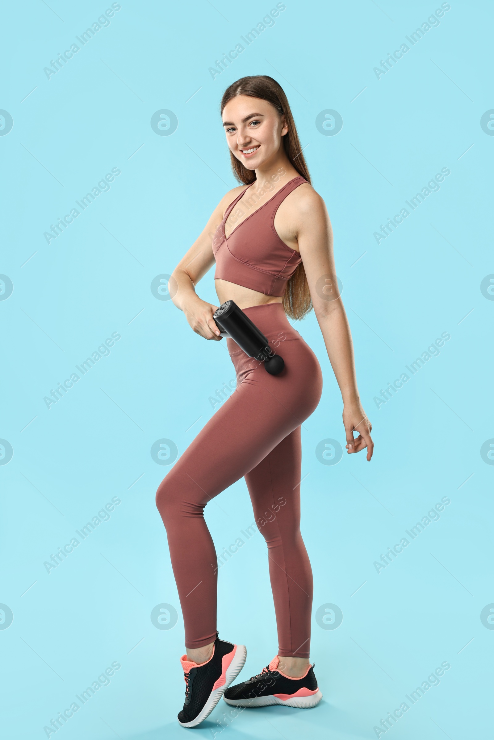 Photo of Woman using percussive massager to relax hip muscles on light blue background