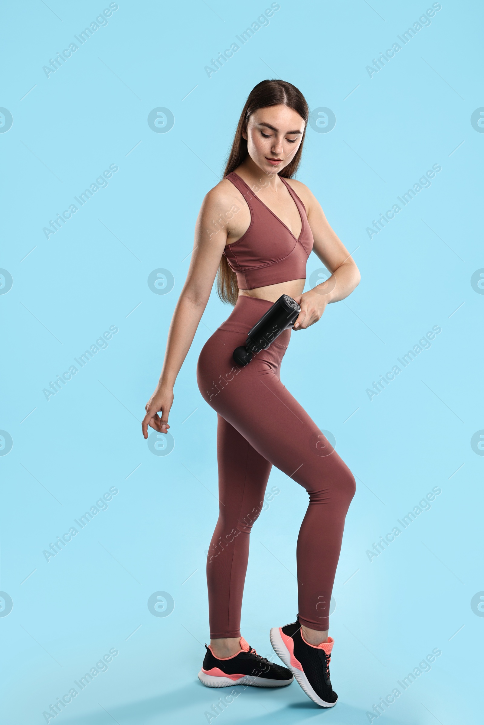 Photo of Woman using percussive massager to relax hip muscles on light blue background