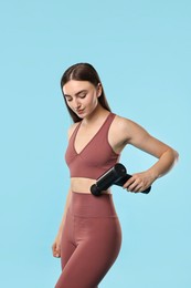 Woman using percussive massager to relieve abdominal muscles on light blue background