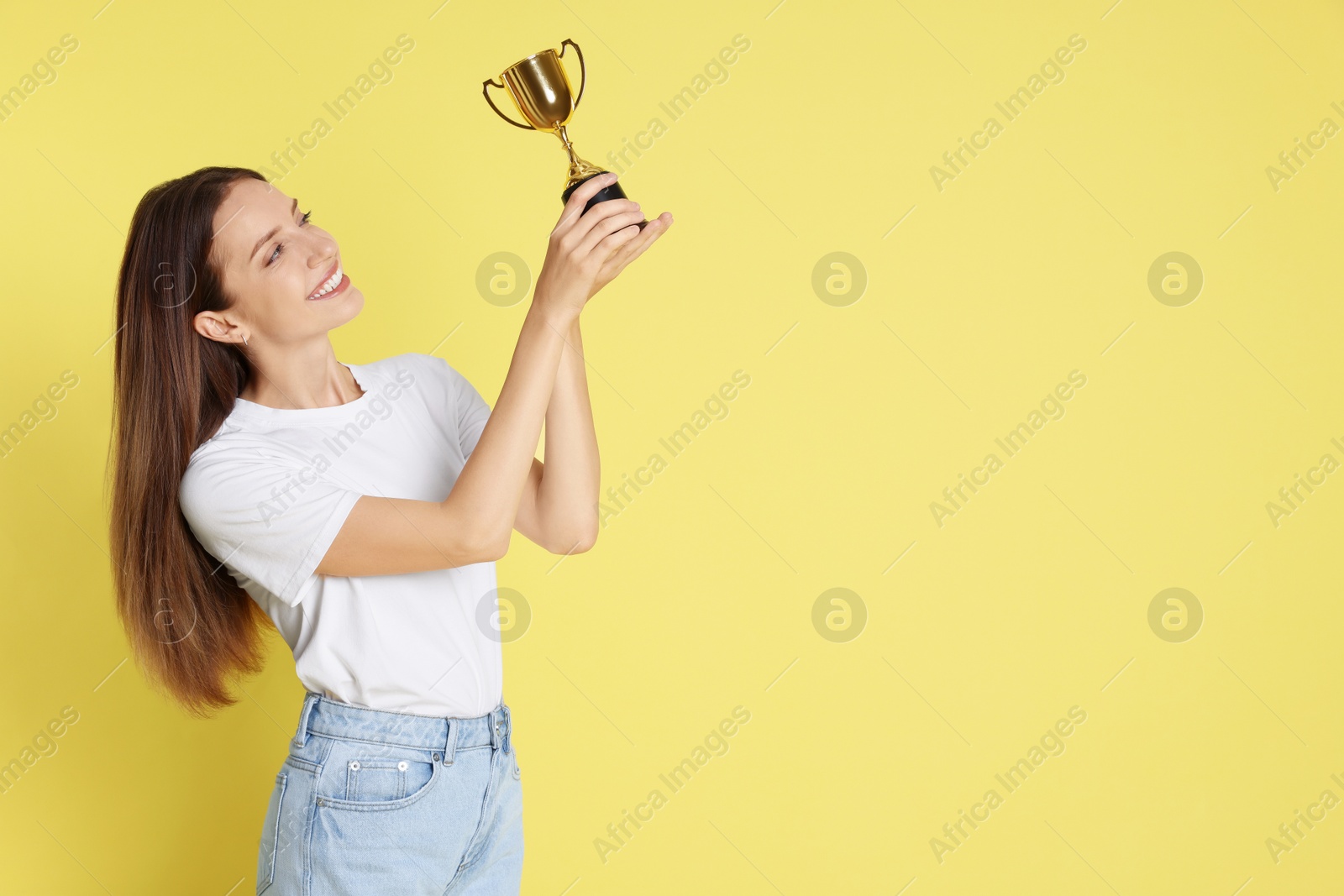 Photo of Happy winner with gold trophy cup on yellow background, space for text