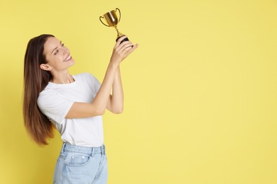 Photo of Happy winner with gold trophy cup on yellow background, space for text