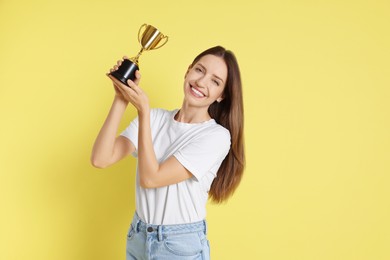 Photo of Happy winner with gold trophy cup on yellow background