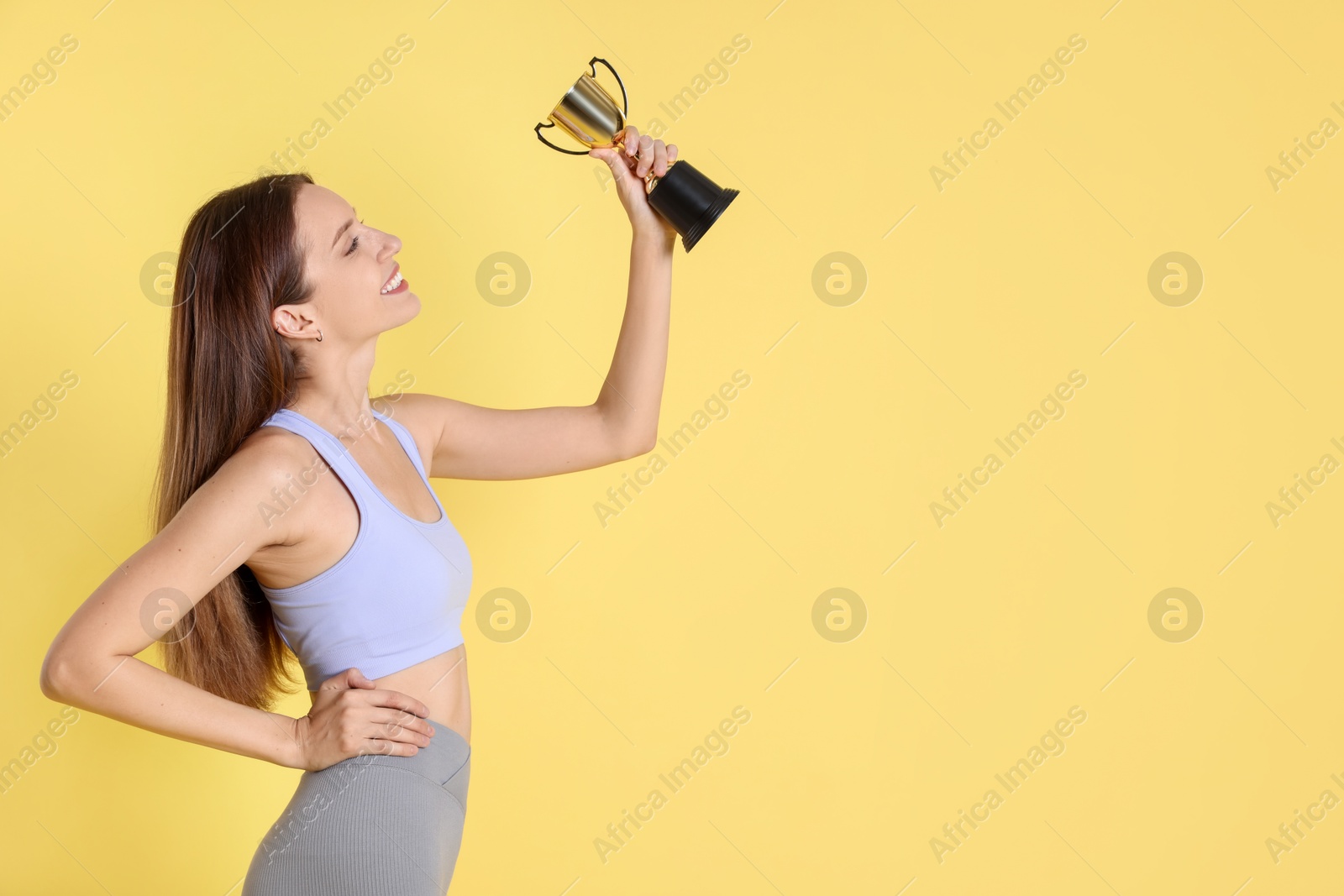 Photo of Happy winner with gold trophy cup on yellow background, space for text