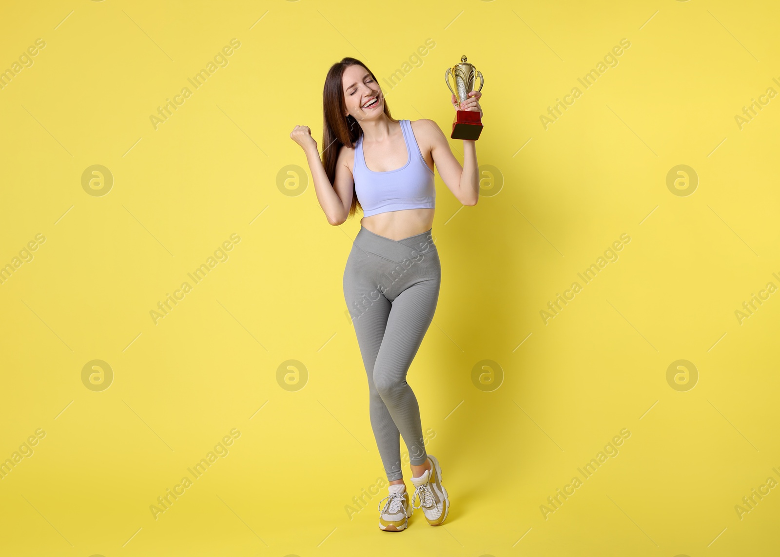 Photo of Happy winner with gold trophy cup on yellow background